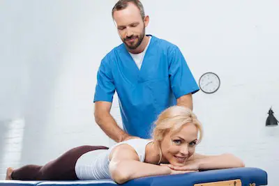 massage therapist doing massage to smiling woman on massage table in clinic